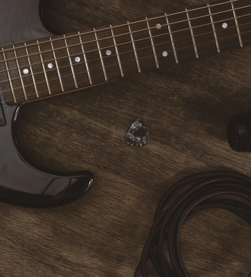 Close-up of an electric guitar, pick, and coiled cable on a wooden surface